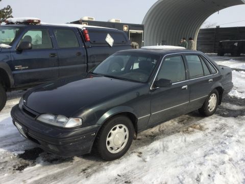 1995 Holden Astra - A dark sedan sits in the snow next to a pickup truck, with a large arched structure behind them.