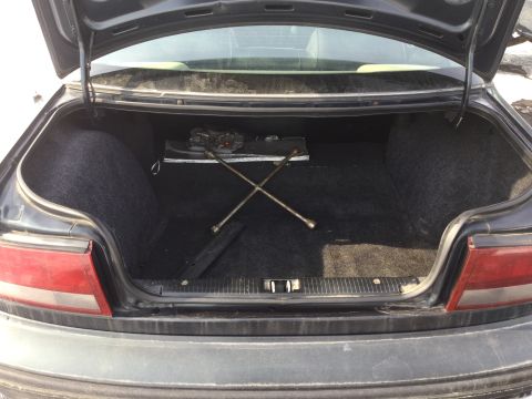 1995 Holden Astra - The trunk of a car is open, revealing the spare tire tools and jack stored inside.