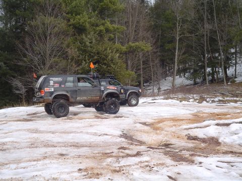 1993 Ford Bronco - Two modified SUVs navigate a snowy trail, one clearly marked as an Explorer, suggesting off-road capabilities.
