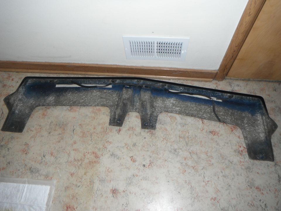 Car part, possibly a bumper or air dam, lying on a patterned floor