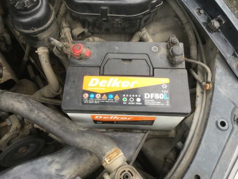 1995 Holden Astra - Close-up view of a Delkor DF80L 12V car battery under the hood of a vehicle.