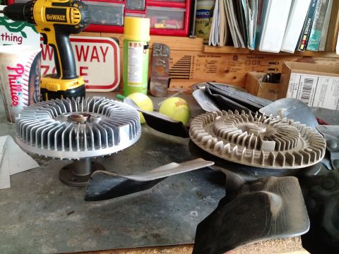 1992 Ford Bronco - Two fan clutches and a fan blade are displayed on a workbench, alongside a yellow drill and tennis balls.