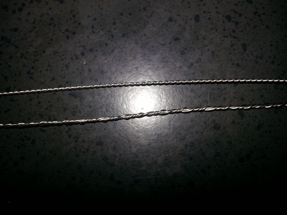 Two twisted metal wires, one thinner than the other, on a dark speckled surface