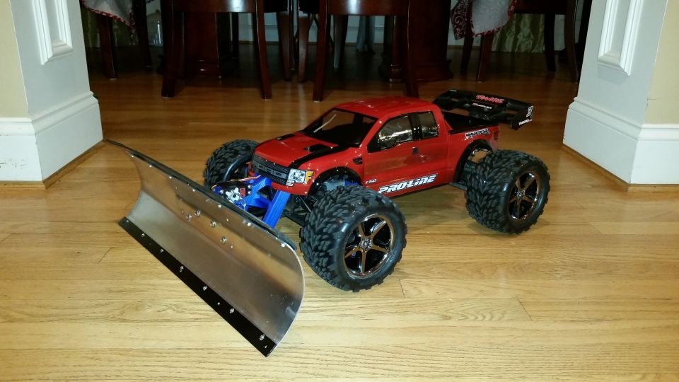 Red RC monster truck with a metal snow plow attached to the front