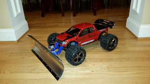 1994 Ford Bronco - A red remote control monster truck is equipped with a snow plow attachment and sits on a wooden floor.