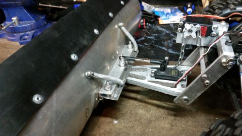 1994 Ford Bronco - Close-up view of a custom snow plow attachment for an RC car, servo motors and mechanical linkages.