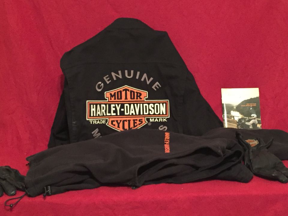 Black Harley-Davidson jacket, pants, and gloves laid out on a red surface with a small booklet