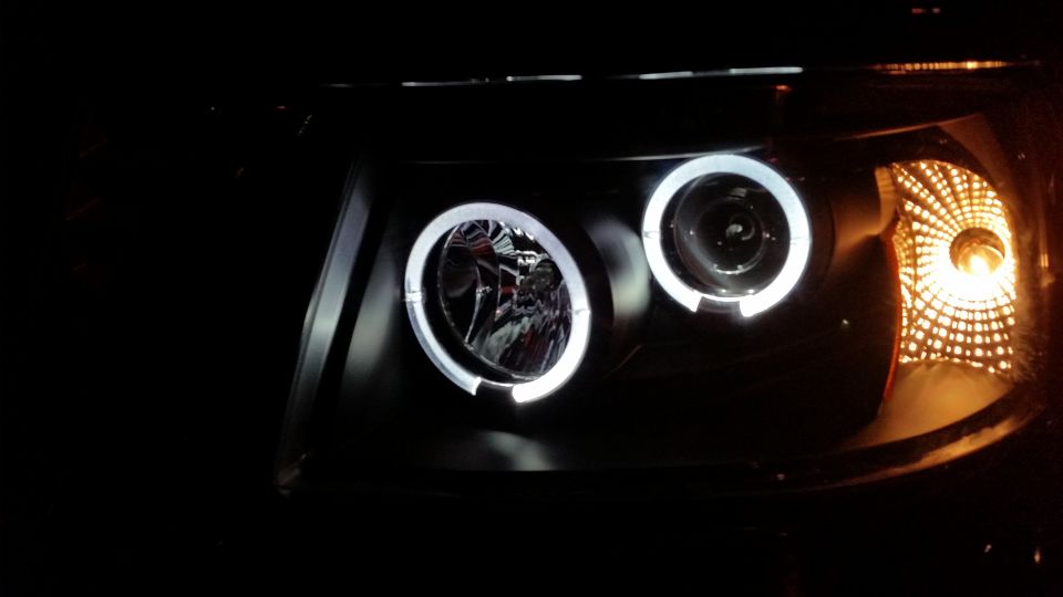 Headlight assembly with dual projector beams and halo rings, one amber turn signal visible