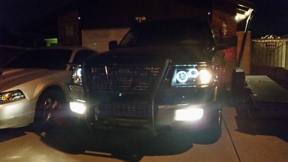 Front view of a dark Ford F-150 truck with halo headlights parked next to a white Ford Mustang