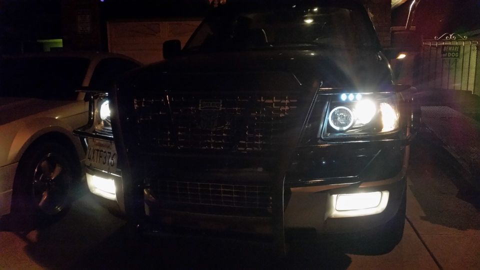 Black Ford F-150 truck front grille with aftermarket halo headlights and fog lights, license plate 4XTF376
