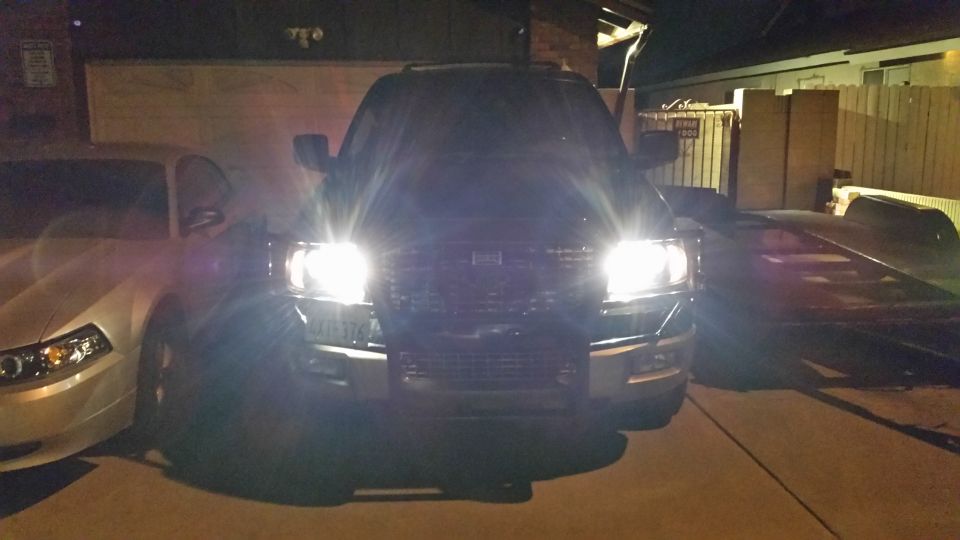 2003 Ford Expedition front view with aftermarket headlights on, parked next to a white car