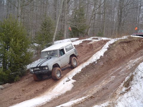 1993 Ford Bronco - Ford Bronco tackling an off-road trail with mud and snow. Another vehicle is partially visible in the distance.