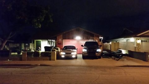 2003 Ford Crown Victoria - silver sedan and a dark SUV are parked in a driveway in front of a single-story house at night, headlights illuminated.