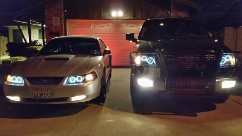 2003 Ford Crown Victoria - silver Ford Mustang and a black SUV with a brush guard are parked in a driveway at night with halo headlights illuminated.