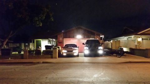 2003 Ford Crown Victoria - silver car and a dark SUV with headlights on are parked in a driveway in front of a house on a residential street at night.