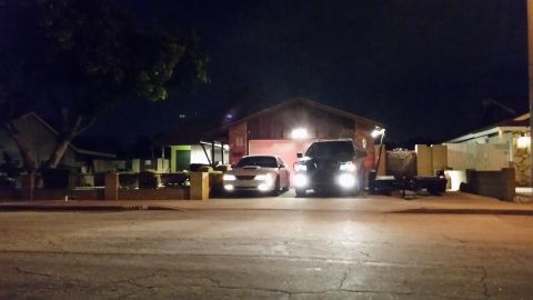 2003 Ford Crown Victoria - silver car and a dark SUV with headlights illuminated sit in a driveway in front of a house, viewed from across the street at night.