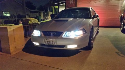 2002 Ford Mustang - A silver 2002 Ford Mustang is parked in front of a garage door at night, with its headlights illuminated.