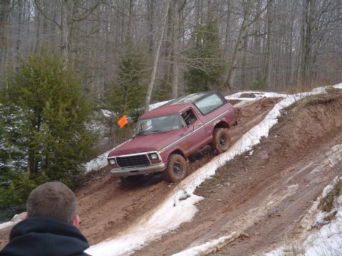 1993 Ford Bronco - A maroon Ford Bronco navigates a challenging muddy incline with patches of snow.