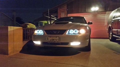 2002 Ford Mustang - A white 2002 Ford Mustang is parked in front of a garage at night, with another vehicle visible to the right.