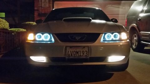 2002 Ford Mustang - A white 2002 Ford Mustang is parked in front of a garage, with a second vehicle to its right.