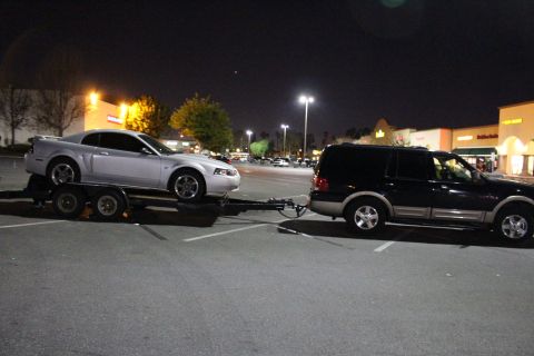 2002 Ford Mustang - A silver Ford Mustang is towed by a black SUV in a parking lot at night.