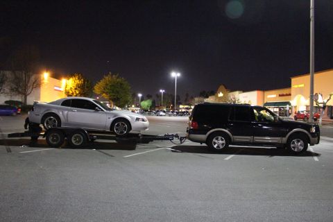 2002 Ford Mustang - A 2002 Ford Mustang is transported on a trailer by a black SUV in a parking lot at night.