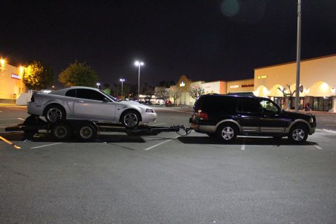 2002 Ford Mustang - A silver Ford Mustang is towed by a dark SUV in a parking lot at night, with store lights in the background.