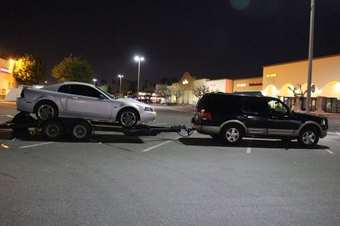 2002 Ford Mustang - A silver 2002 Ford Mustang is being towed by a black SUV in a parking lot at night.