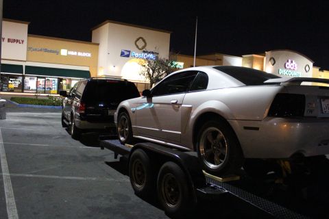 2002 Ford Mustang - White 2002 Ford Mustang coupe is loaded onto a trailer, with a black SUV behind it.