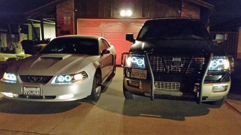 2002 Ford Mustang - A silver 2002 Ford Mustang is parked next to a dark SUV in front of a garage.