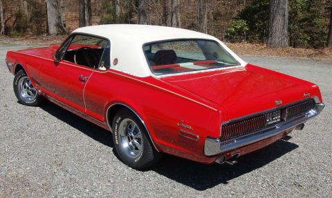 1968 Mercury Cougar - A red 1968 Mercury Cougar with a white vinyl roof is parked on a gravel surface.
