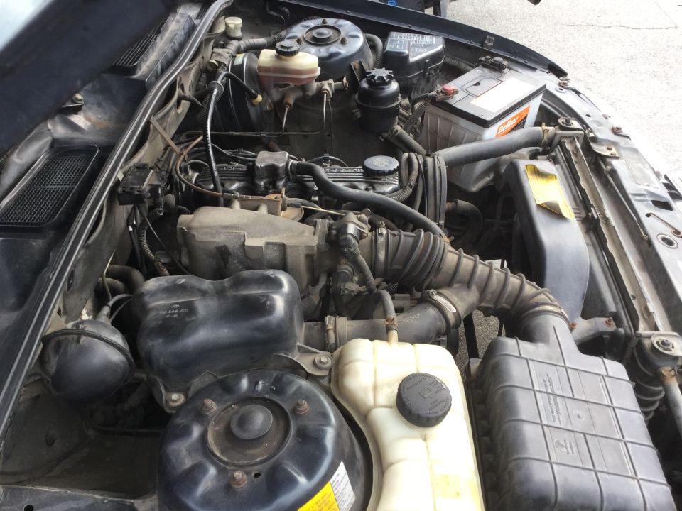 Engine bay with various hoses, battery, and engine components visible