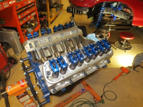 1996 Ford Bronco - V8 engine block with blue valve covers and exposed pushrods sits on an engine stand in a garage.
