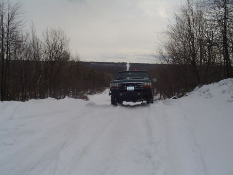 1993 Ford Bronco - A dark green SUV navigates a snow-covered road, its front grille and bumper clearly visible.