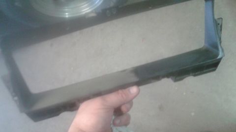 1996 Ford Bronco - A person holds a black plastic automotive grille frame, with a fan or radiator component visible in the background.