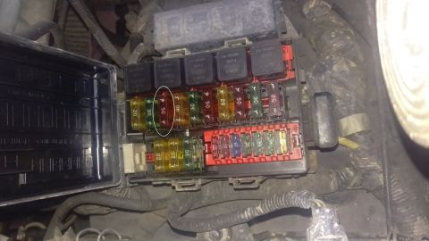 1994 Ford Bronco - Close-up of an automotive fuse box, showing an array of fuses and relays, with a protective cover ajar.