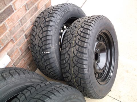 1999 Mercury Grand Marquis - Four General Arctic tires on black steel wheels are shown leaning against a brick wall.