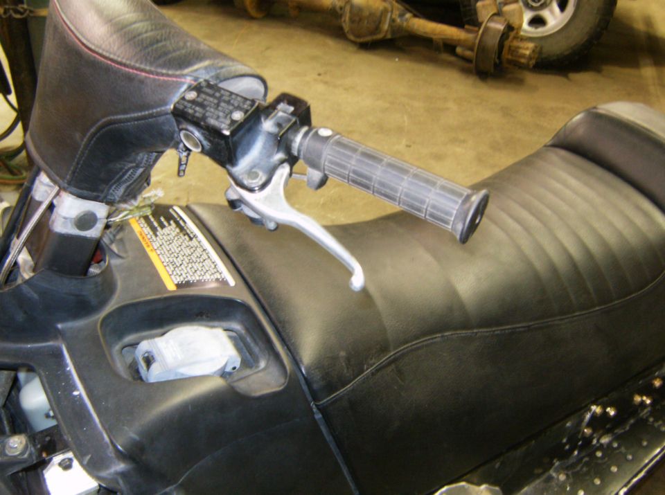 Snowmobile handlebars, brake lever, and seat. A rear axle assembly is visible in the background