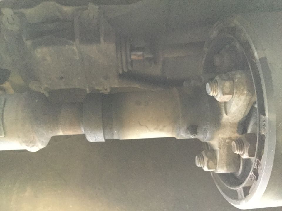 Close-up of a vehicle's driveshaft connected to a brake drum assembly with visible bolts and nuts