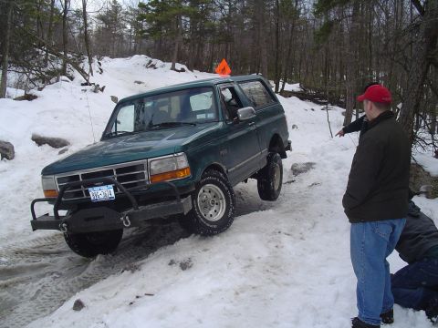 1993 Ford Bronco - A green Ford Bronco navigates a snowy, wooded trail with two people observing.