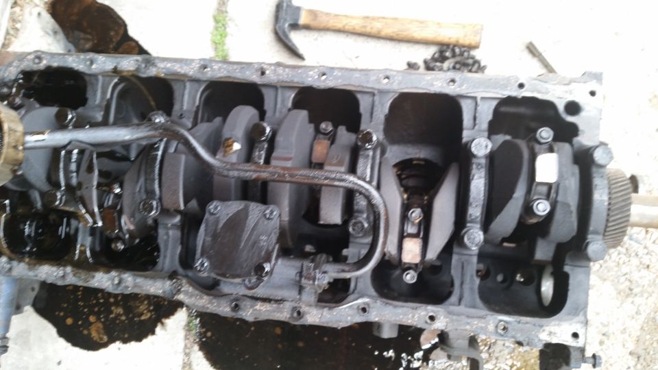 Engine block with crankshaft and connecting rods, viewed from above. A hammer rests in the background