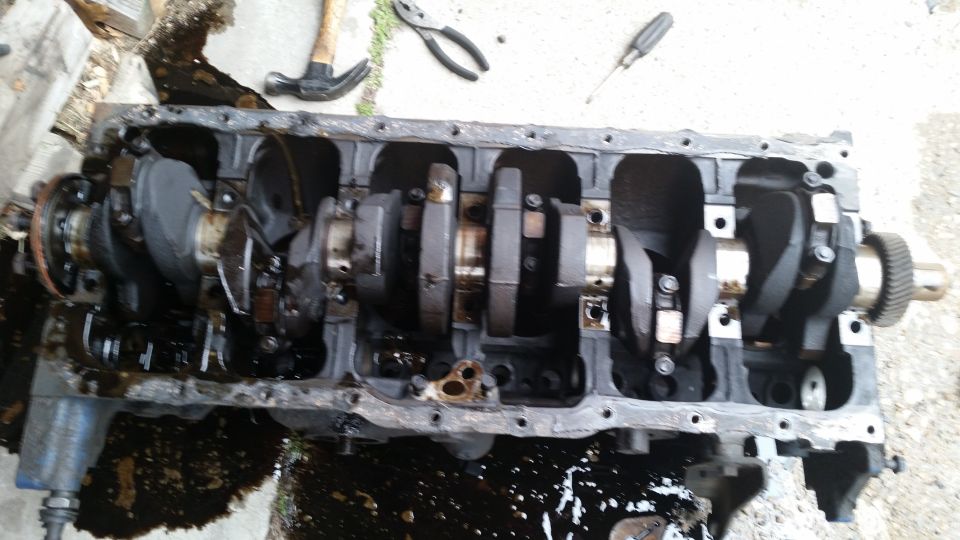 Engine block with crankshaft and connecting rods visible. Tools like a hammer, pliers, and screwdriver are nearby
