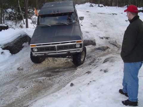 1993 Ford Bronco - A dark 1977 Ford Bronco navigates a challenging snowy and rocky terrain with a spectator watching.