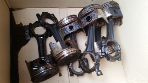 1981 Ford Bronco - Several used pistons and connecting rods are shown in a cardboard box, some with visible damage and oil residue.