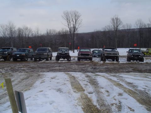 1993 Ford Bronco - Multiple SUVs and trucks are parked in a snowy outdoor area with trees visible.
