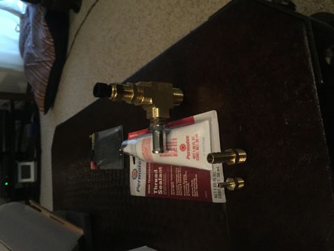 1982 Ford Bronco - Plumbing fittings and thread sealant are laid out on a dark surface.