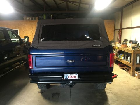 1982 Ford Bronco - Rear view of a blue Ford Bronco with a soft top, parked in a garage next to another vehicle.