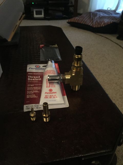 1982 Ford Bronco - Plumbing fittings and thread sealant are laid out on a dark surface.