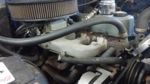 1985 Ford Bronco - Close-up view of an engine bay, showing the carburetor, air filter, and exhaust manifold. Some text is visible on a sticker.