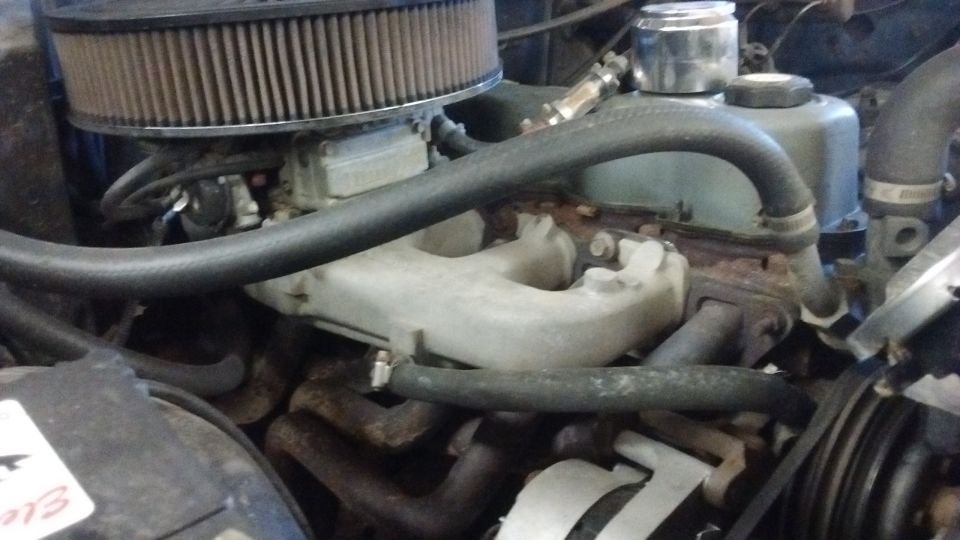 Engine bay with carburetor and exhaust manifold. Readable text on sticker